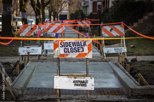 Sidewalk closed for construction blocked by orange and white warning sign
