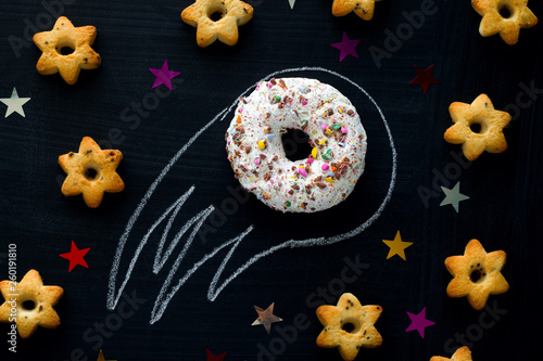 donut meteorite among the stars of cookies on a black chalkboard background, funny children's entertainment with food, space concept