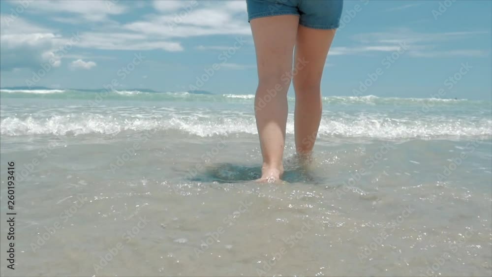 On a Tropical Beach Close-Up of Women's Legs European Cute Brunette Goes Under the Hot Summer Sun Along the Tropical Exotic Coast, Carefree Girl Walking on the Sand Right to the Ocean, Slow Motion. On a Tropical Beach Close-Up of Women's Legs European Cute Brunette Goes Under the Hot Summer Sun Along the Tropical Exotic Coast, Carefree Girl Walking on the Sand Right to the Ocean, Slow Motion.