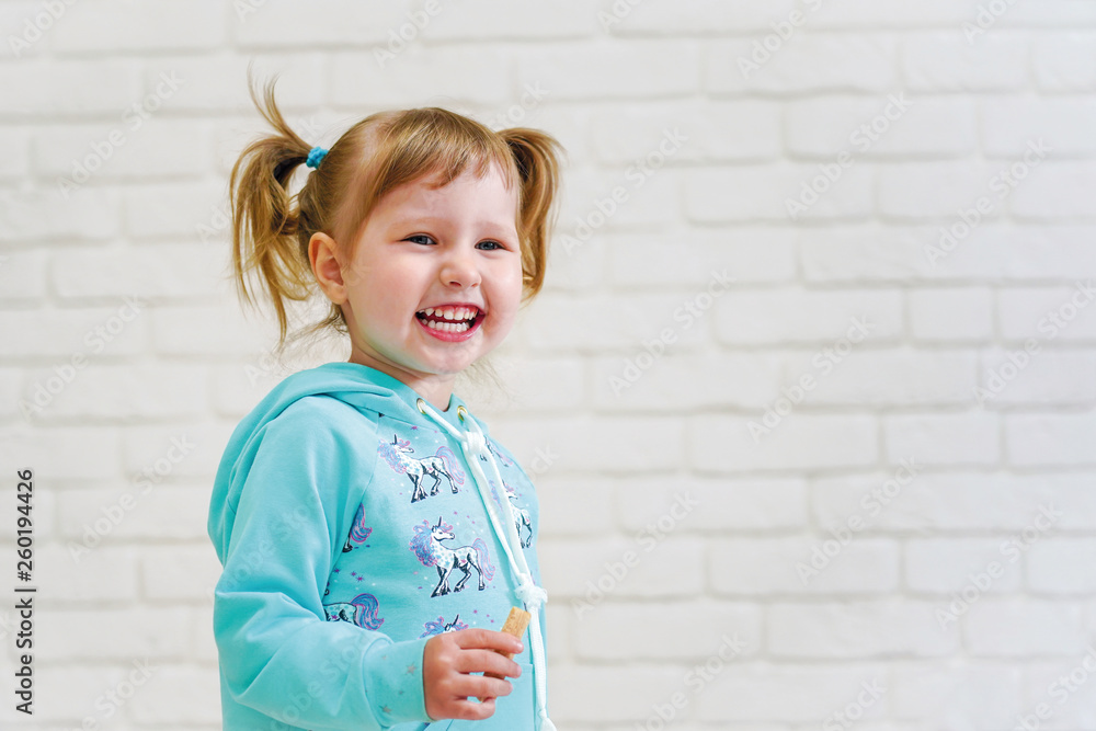 happy girl with pigtails laughing in front of a white brick wall