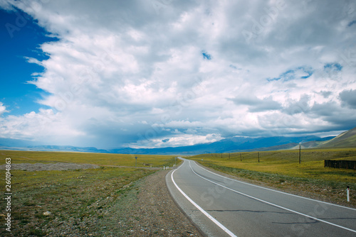 A winding road running in a mountainous area. Smooth asphalt road passes between the yellow plain to the distant mountains. The Chui highway through the kurai steppe, Altai. Low clouds over the road.