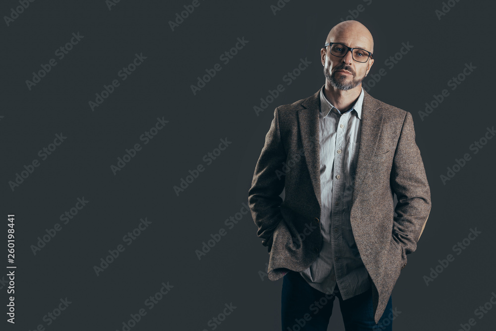 Serious middle aged man with a deadpan face expression dressed in casual posing on a dark gray background Serious middle aged man with a deadpan face expression dressed in casual posing on a dark gray background