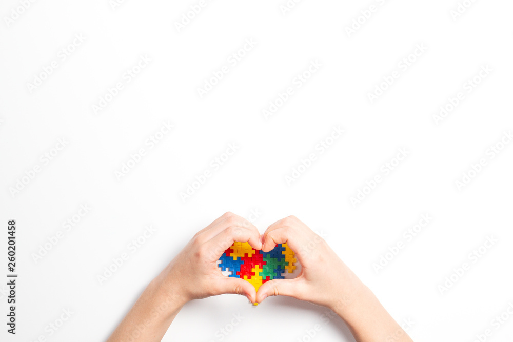 Kid hands in the shape of heart and colorful heart made of plastic construction puzzle pieces on white background. World autism awareness day concept Kid hands in the shape of heart and colorful heart made of plastic construction puzzle pieces on white background. World autism awareness day concept