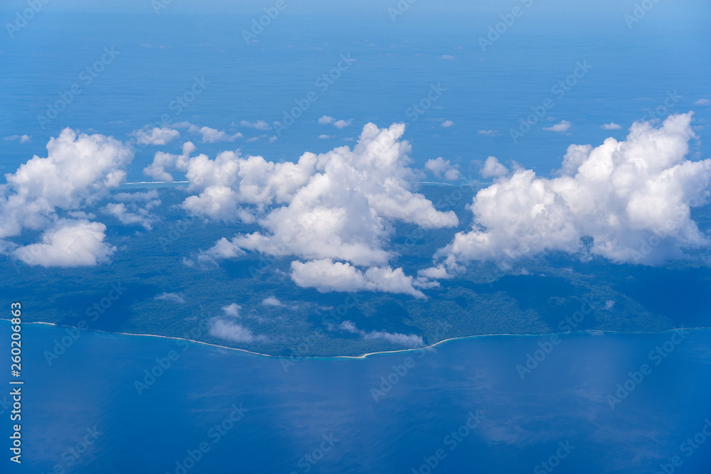 Beautiful view from window of plane flying over white clouds, sea surface and island. Natural panorama with clouds, water surface of sea and land