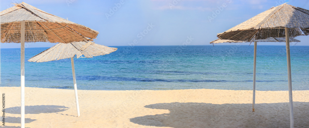 Fototapeta premium Beach umbrellas and clean sand against the backdrop of the azure coast of the sea. Vacation and Tourism concept.