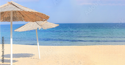 Beach umbrellas and clean sand against the backdrop of the azure coast of the sea. Vacation and Tourism concept. © Oleksandra