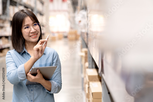 Candid or headshot of young happy attractive asian employee or staff working in store inventory in warehouse using computer tablet. Asian small business owner concept smile and point hands to shelf.