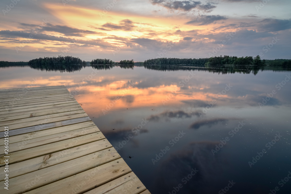 Wooden jetty on still lake with forest horizon with vibrant color sky from sunset