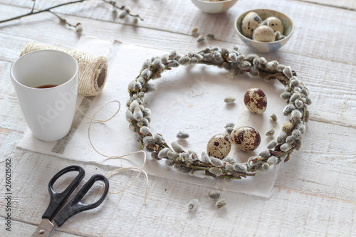 Making pussy willow wreath and decorating with quail eggs as a symbols of spring and Easter on a white wooden table