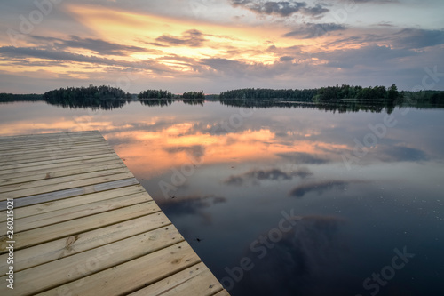Wooden jetty on still lake with forest horizon with vibrant color sky from sunset