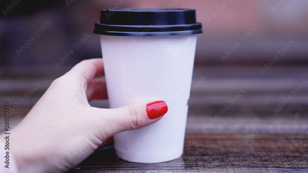 Cup of coffee on a wooden table in female hands. Paper cup Plastic cap. Beautiful hands with red nails Cup of coffee on a wooden table in female hands. Paper cup Plastic cap. Beautiful hands with red nails