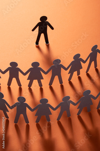 Paper human figure standing in front of paper people holding hands on red surface. Bulling, segregation, conflict concept.