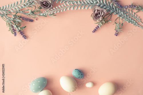 Creative layout made with spring flowers leaves and Easter eggs on pastel pink background. Minimal nature composition.