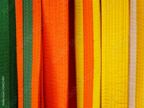 Closeup of martial arts belts for karate or kickboxing - white with yellow tag, yellow, yellow with orange tag, orange, orange with green tag, green