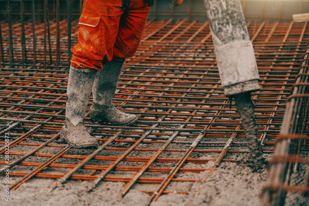 Construction site worker in boots and orange protective suit pouring concrete. Construction site worker in boots and orange protective suit pouring concrete.