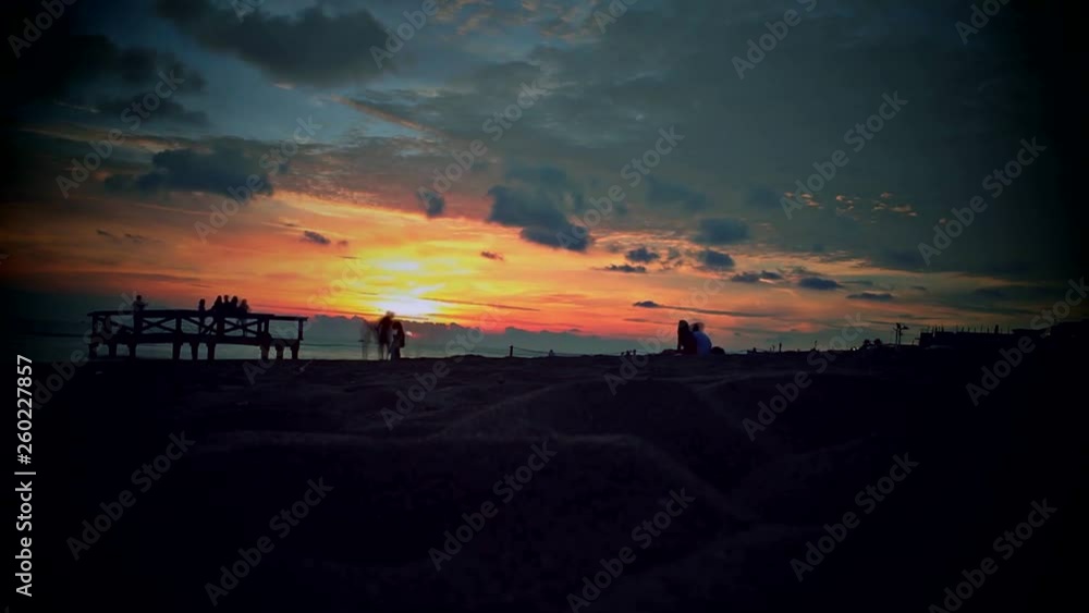 Time lapse of a sunset on the beach with silhouette of people in motion and taking selfies on a bridge by the sea Time lapse of a sunset on the beach with silhouette of people in motion and taking selfies on a bridge by the sea