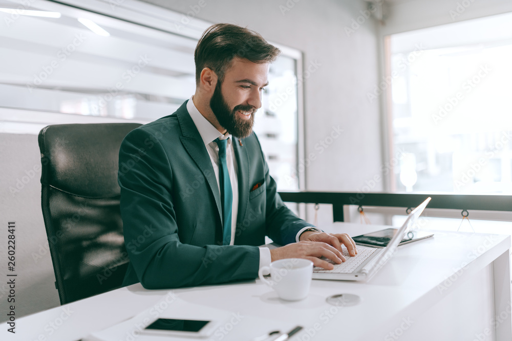 Fototapeta premium Happy Caucasian bearded businessman in formal wear using laptop in office. A winner is a dreamer who never quits.