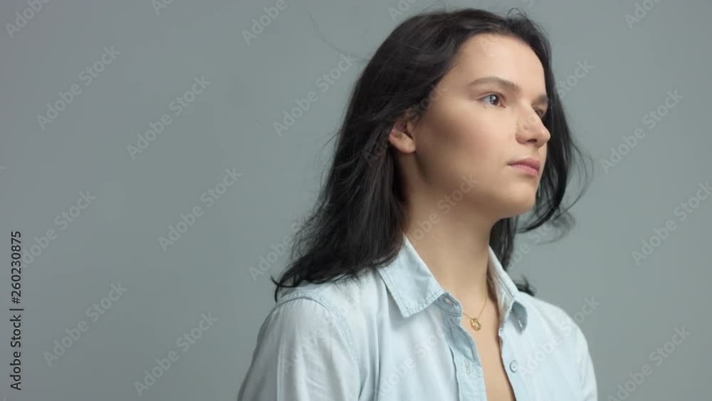 Brunette in studio portrait video shoot wwears jeans shirt with blowing hair slow motion from 60 fps Calm brunette portrait watching aside, touches her hair and then turns to the camera Brunette in studio portrait video shoot wwears jeans shirt with blowing hair slow motion from 60 fps Calm brunette portrait watching aside, touches her hair and then turns to the camera