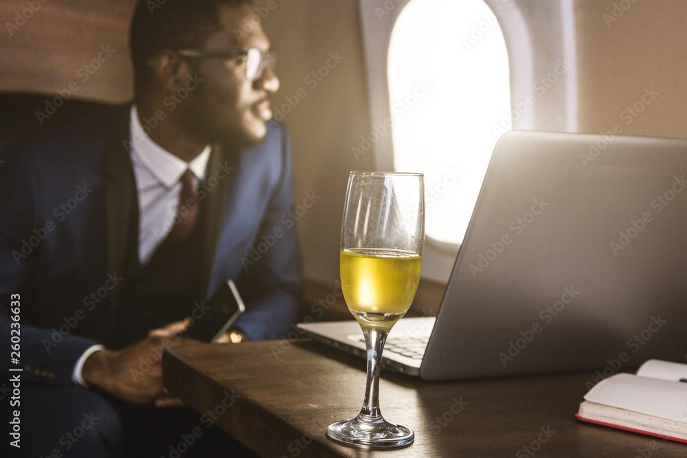 Attractive and successful African American businessman with glasses working on a laptop while sitting in the chair of his private jet.