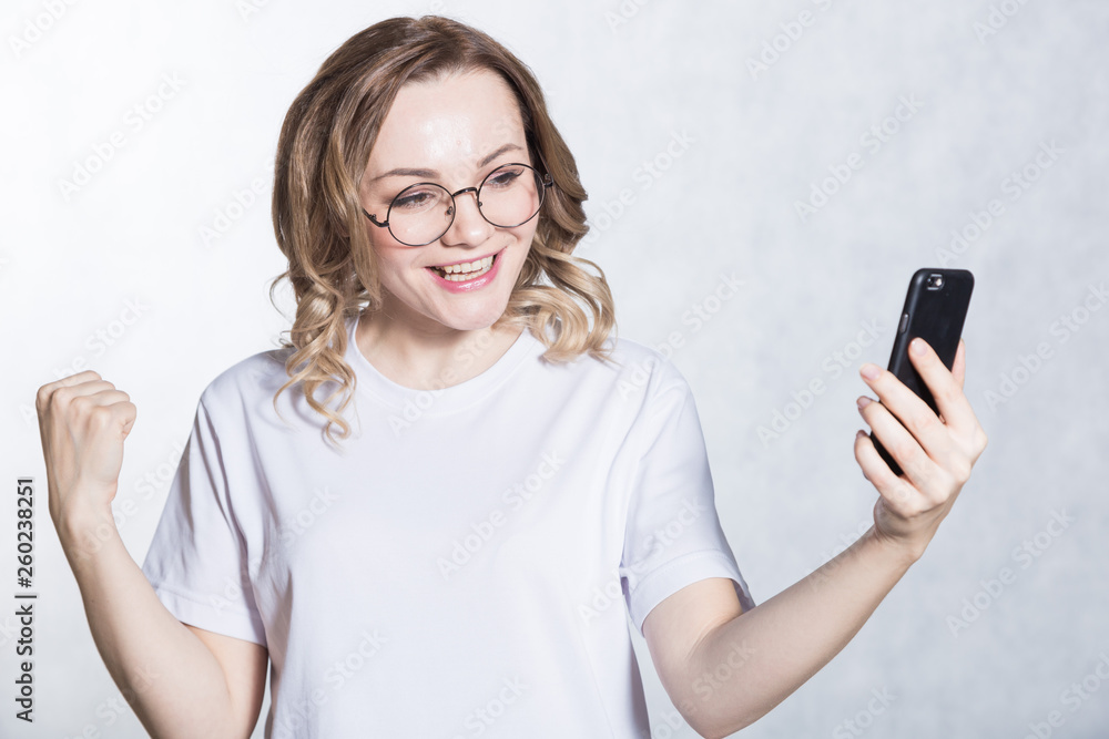 Happy young woman in glasses holding smartphone and celebrating his success. Happy young woman in glasses holding smartphone and celebrating his success.