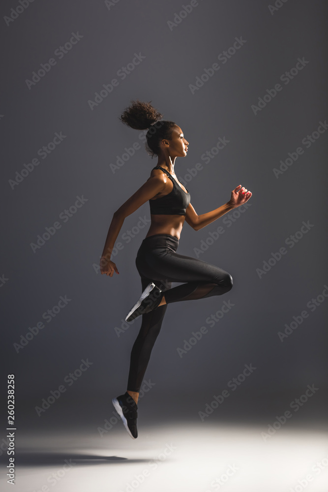 side view of beautiful athletic african american sportswoman jumping on black
