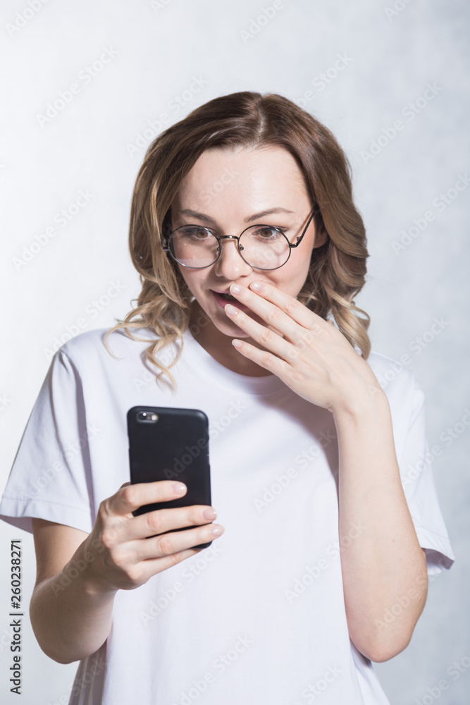 Perplexed and worried, a beautiful young woman is holding a smartphone, stares with surprised expression.