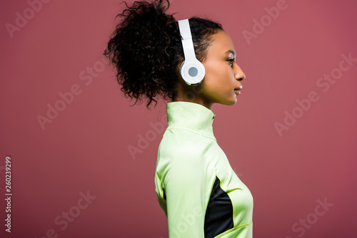 side view of beautiful african american sportswoman in headphones isolated on brown