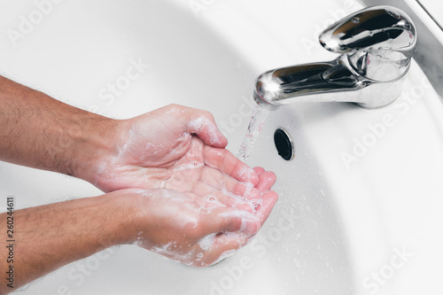 Adult caucasian male washing hands with soap under the faucet with water