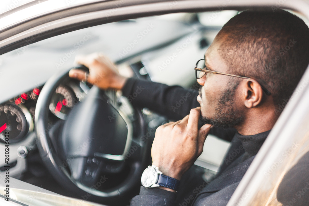 A young businessman in a suit sits at the wheel of a expensive car.