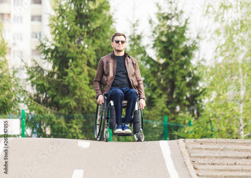 Photo A young man in a wheelchair rides along the park road.