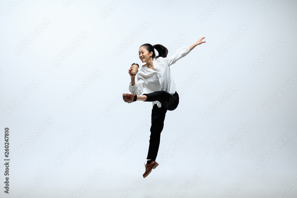 Coffee brings inspiration for a new day. Happy woman working at office, jumping and dancing in casual clothes isolated on white studio background. Business, start-up, working open-space concept.