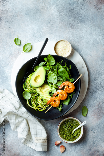 Detox Buddha bowl with avocado, spinach, greens, zucchini noodles, grilled shrimps and pesto sauce. Vegetarian vegetable low carb lunch bowl.