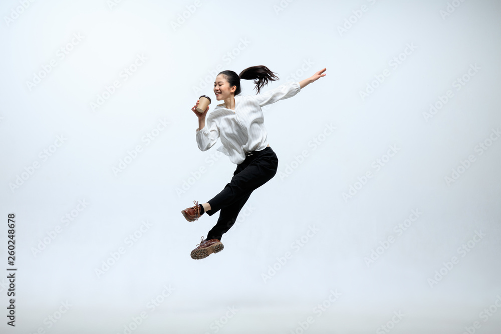 Hurry up to get your coffee. Happy woman working at office, jumping and dancing in casual clothes or suit isolated on white studio background. Business, start-up, working open-space concept.