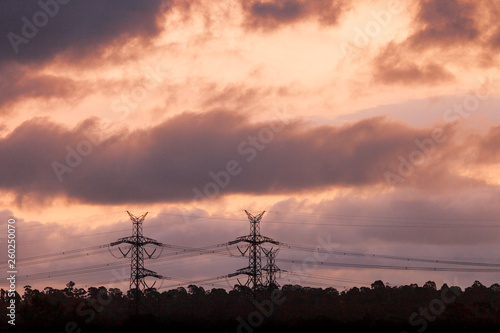 Electricity pylons standing in silhouette behind dusk sunset.