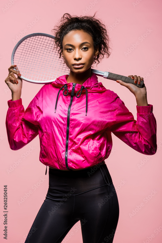 beautiful african american sportswoman with tennis racket posing and looking at camera isolated on pink beautiful african american sportswoman with tennis racket posing and looking at camera isolated on pink
