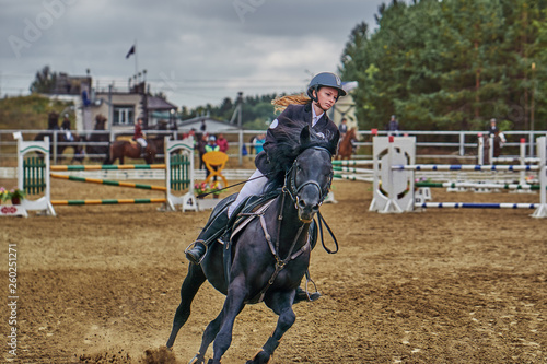 Young woman jockey in white black dress and black boots takes part in equestrian competitions.