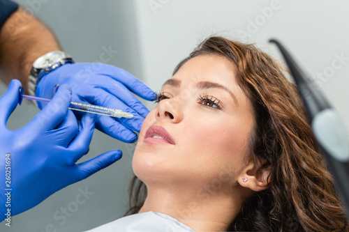 Attractive young woman is getting a rejuvenating facial injections. She is sitting calmly at clinic. The expert beautician is filling female wrinkles by hyaluronic acid.