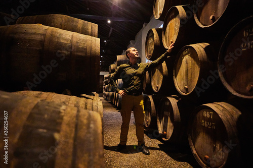 Leinwand Poster Professional winemaker male  in old aged traditional wooden barrels with wine in