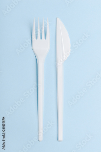 Plastic white disposable fork and knife on a blue background. Concept plastic dishes, fast food, plastic pollution. Top view, flat lay.