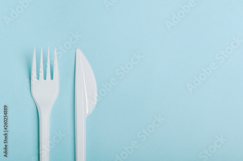 Plastic white disposable fork and knife on a blue background. Concept plastic dishes, fast food, plastic pollution. Copy space, top view, flat lay