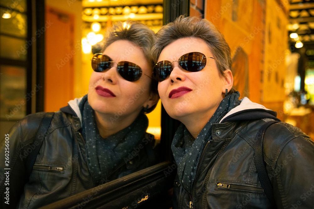 Spain, Barcelona, cafe, 14 March 2019. Girl with short hair and dark glasses standing near the mirror and admires his reflection. Spain, Barcelona, cafe, 14 March 2019. Girl with short hair and dark glasses standing near the mirror and admires his reflection.