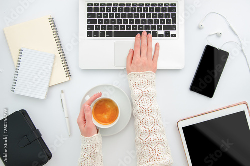 Workplace top view white desktop with gadgets, phone, tablet and female hands are typing on a laptop