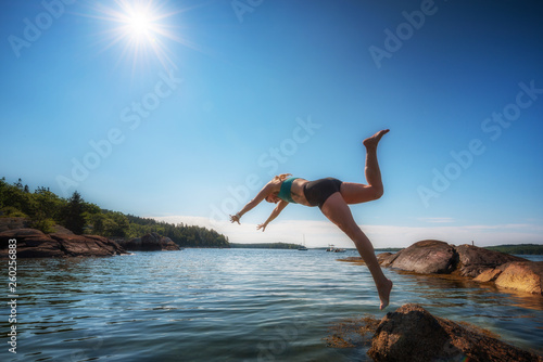 Woman diving in to the ocean off of rocks with sun star in the sky.