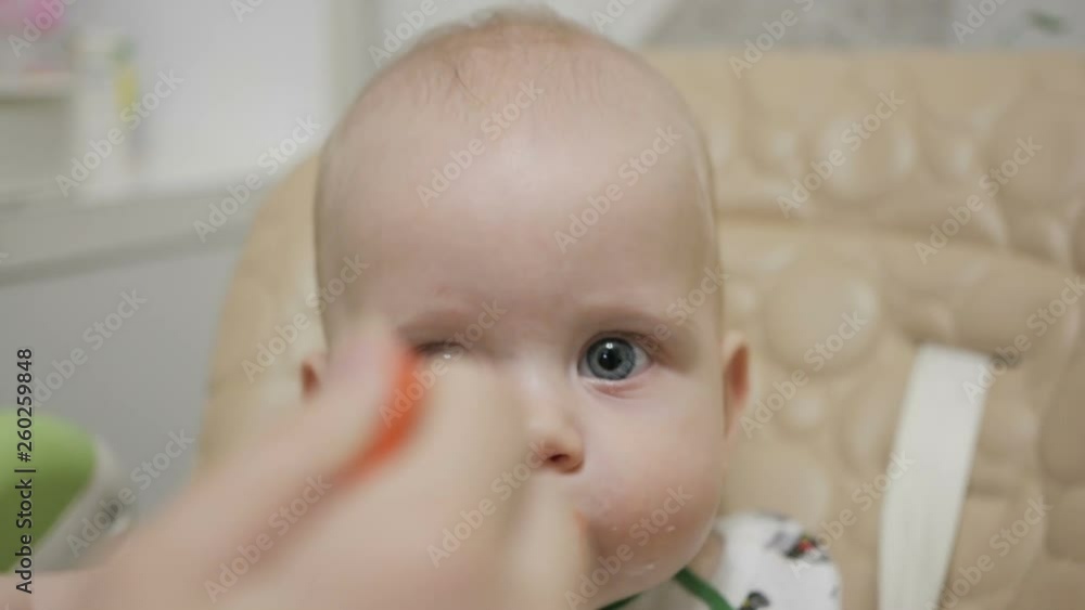 Mother feeding baby with a spoon, close up shot at kitchen. slow motion Mother feeding baby with a spoon, close up shot at kitchen. slow motion