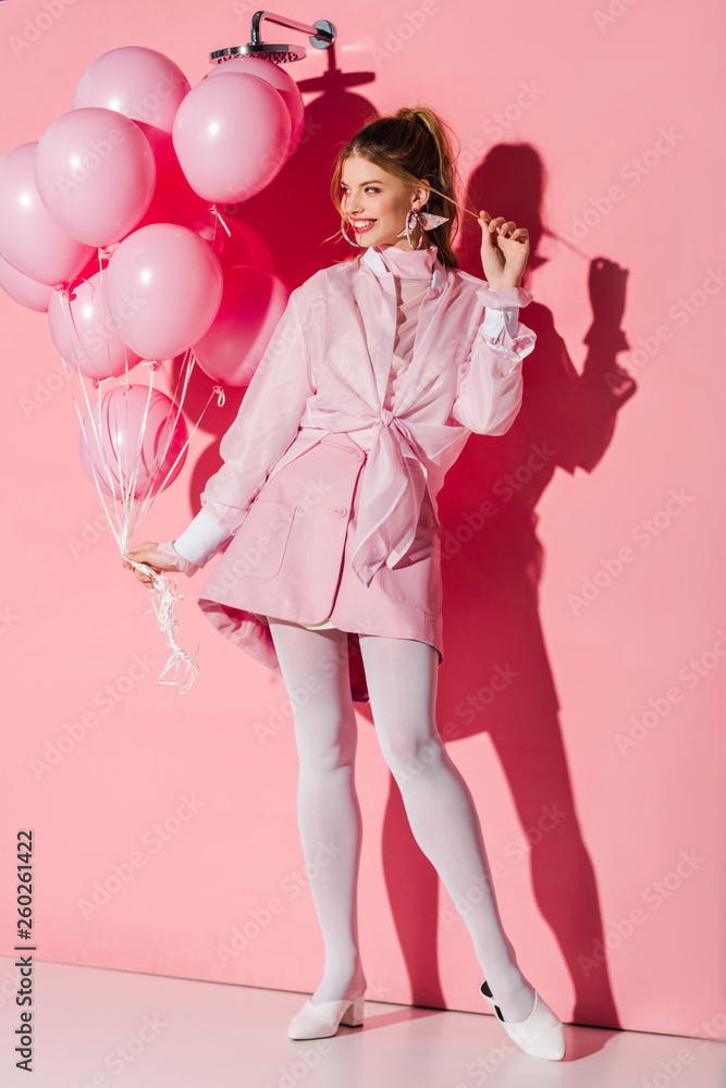 cheerful young woman holding air balloons while touching hair on pink cheerful young woman holding air balloons while touching hair on pink