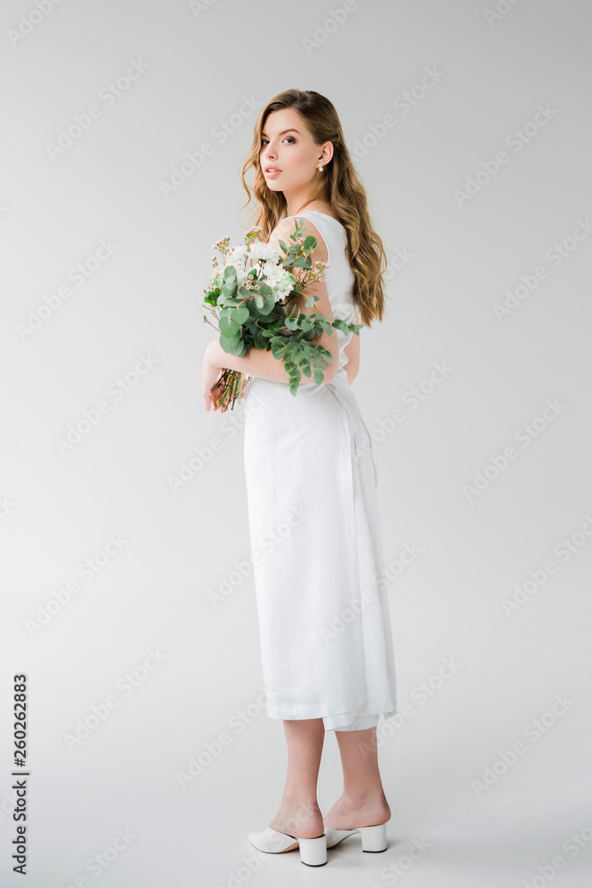 young woman in white dress holding while standing on grey young woman in white dress holding while standing on grey
