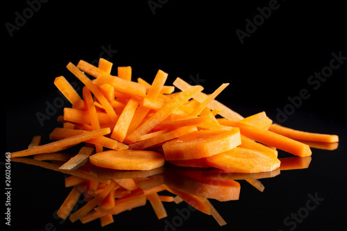 Group of five slices lot of pieces of fresh orange carrot thin noodles and round slices isolated on black glass