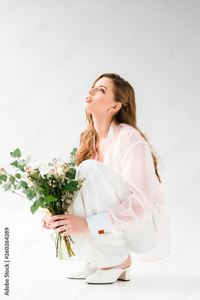 attractive woman holding flowers with green eucalyptus leaves while sitting on white attractive woman holding flowers with green eucalyptus leaves while sitting on white