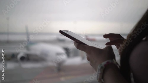 Woman using mobile phone at airport terminal and waiting for boarding the plane