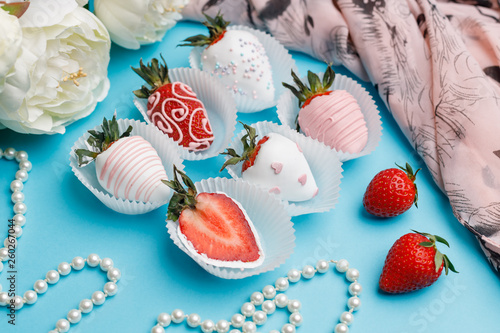Fresh strawberries covered with white and pink chocolate, white flowers and pearl beads lie on a turquoise background